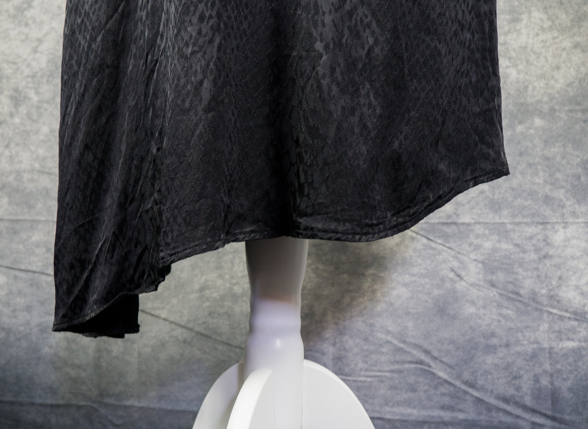 A black textured fabric garment draped over a white mannequin torso against a gray wrinkled backdrop.