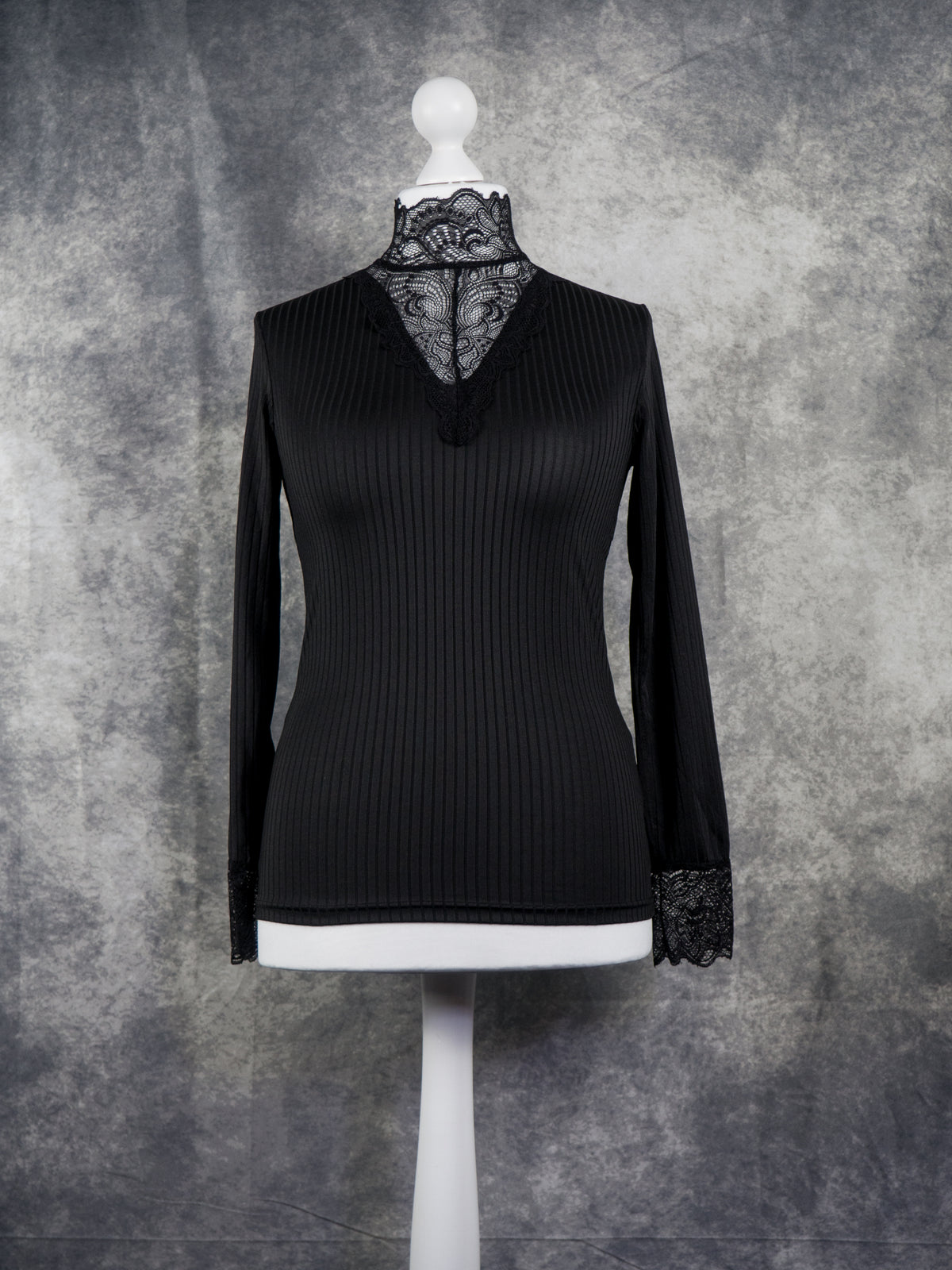 A black long-sleeve ribbed knit top with a lace mock neck and lace cuffs, displayed on a white mannequin torso against a textured gray studio backdrop.
