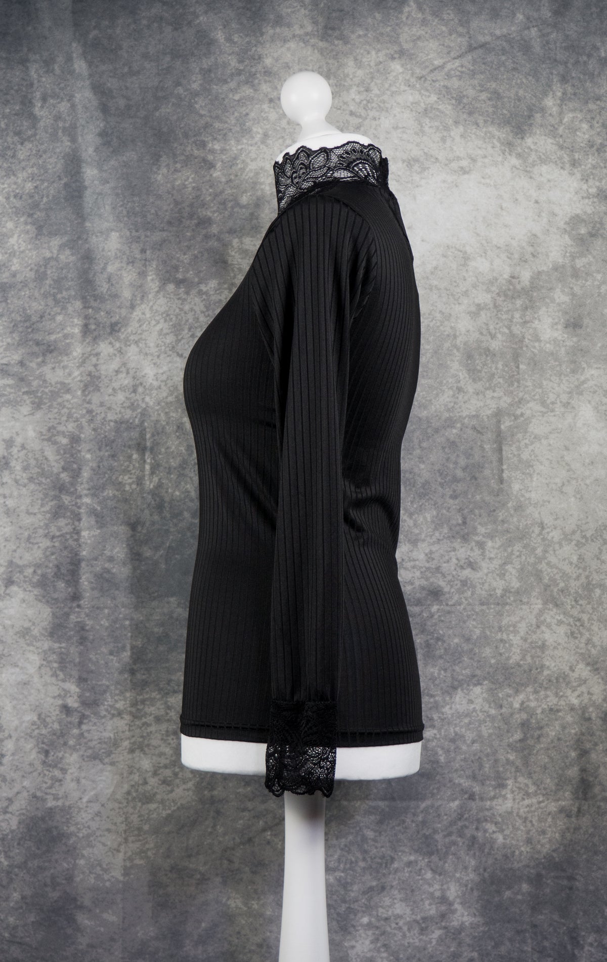 A black long-sleeve ribbed knit top with a lace mock neck and matching lace cuff, displayed on a white mannequin torso against a textured gray studio backdrop.