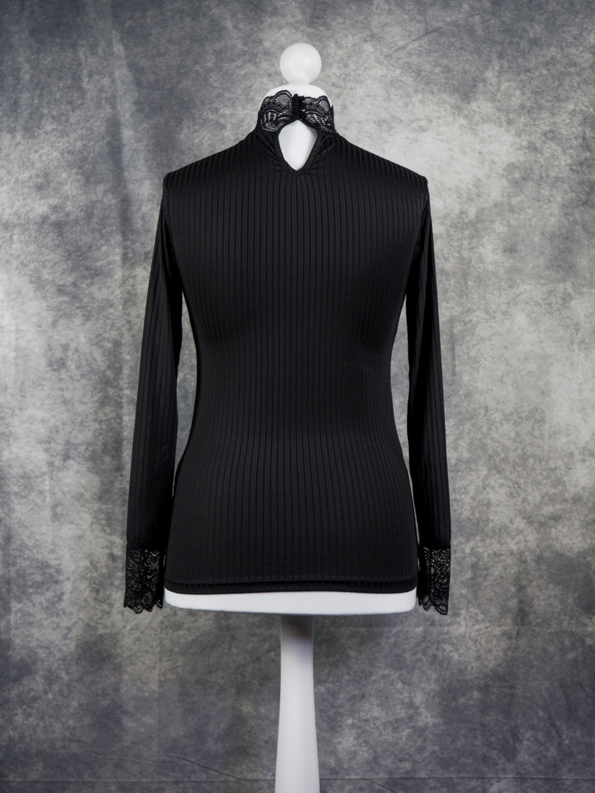A black long-sleeve ribbed mock-neck top with black lace trim at the collar and cuffs, displayed on a white mannequin torso against a textured gray studio background.