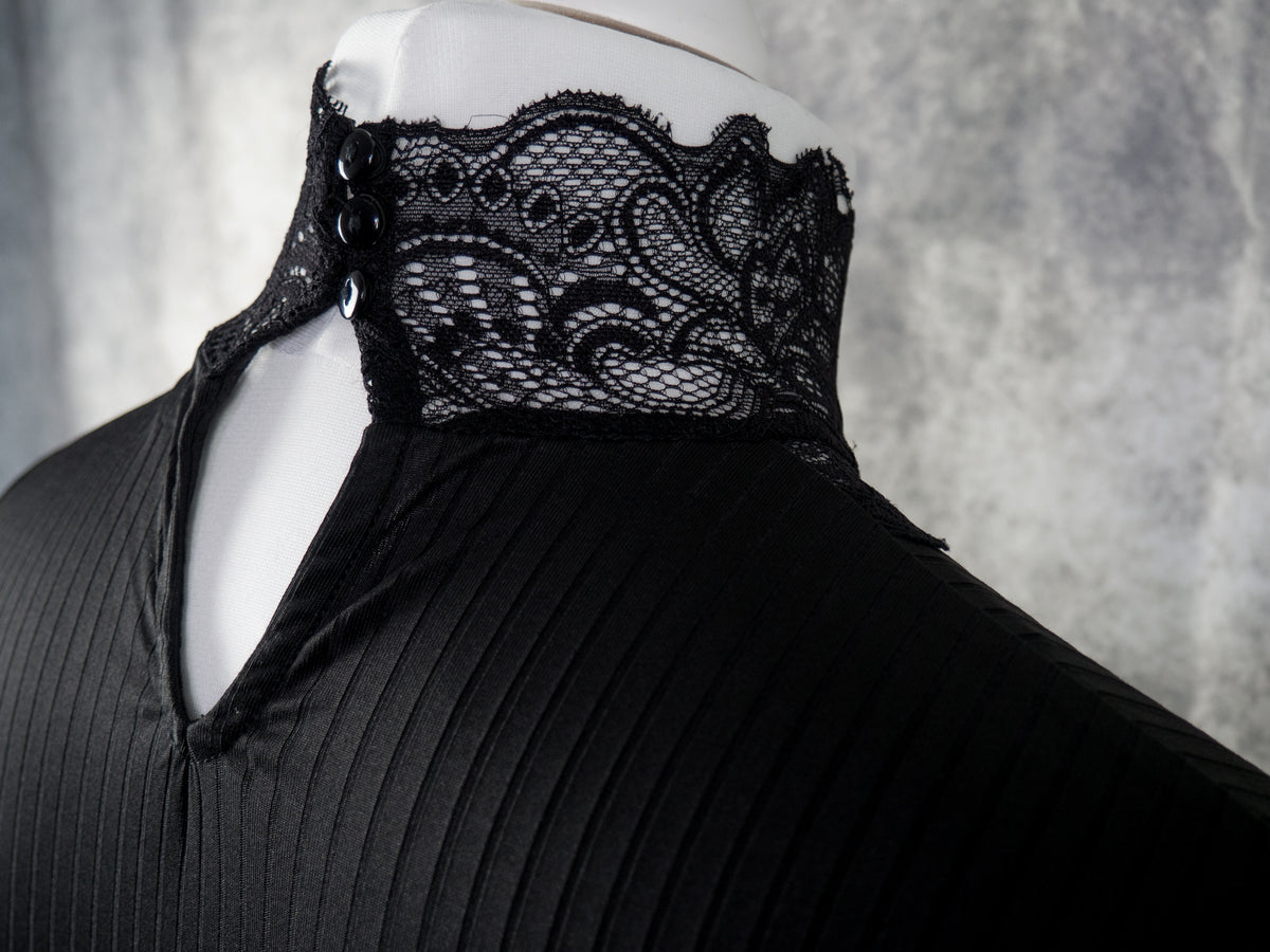 A close-up of a black pleated garment displayed on a white mannequin torso, featuring a high lace collar with decorative buttons and a keyhole cutout at the neckline, set against a textured gray background.