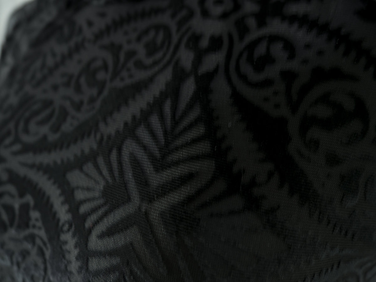 A macro close-up showcasing the detailed texture of the black devoré velvet fabric, highlighting the contrast between the raised plush velvet motifs and the semi-sheer, smooth fabric base of the intricate damask pattern.
