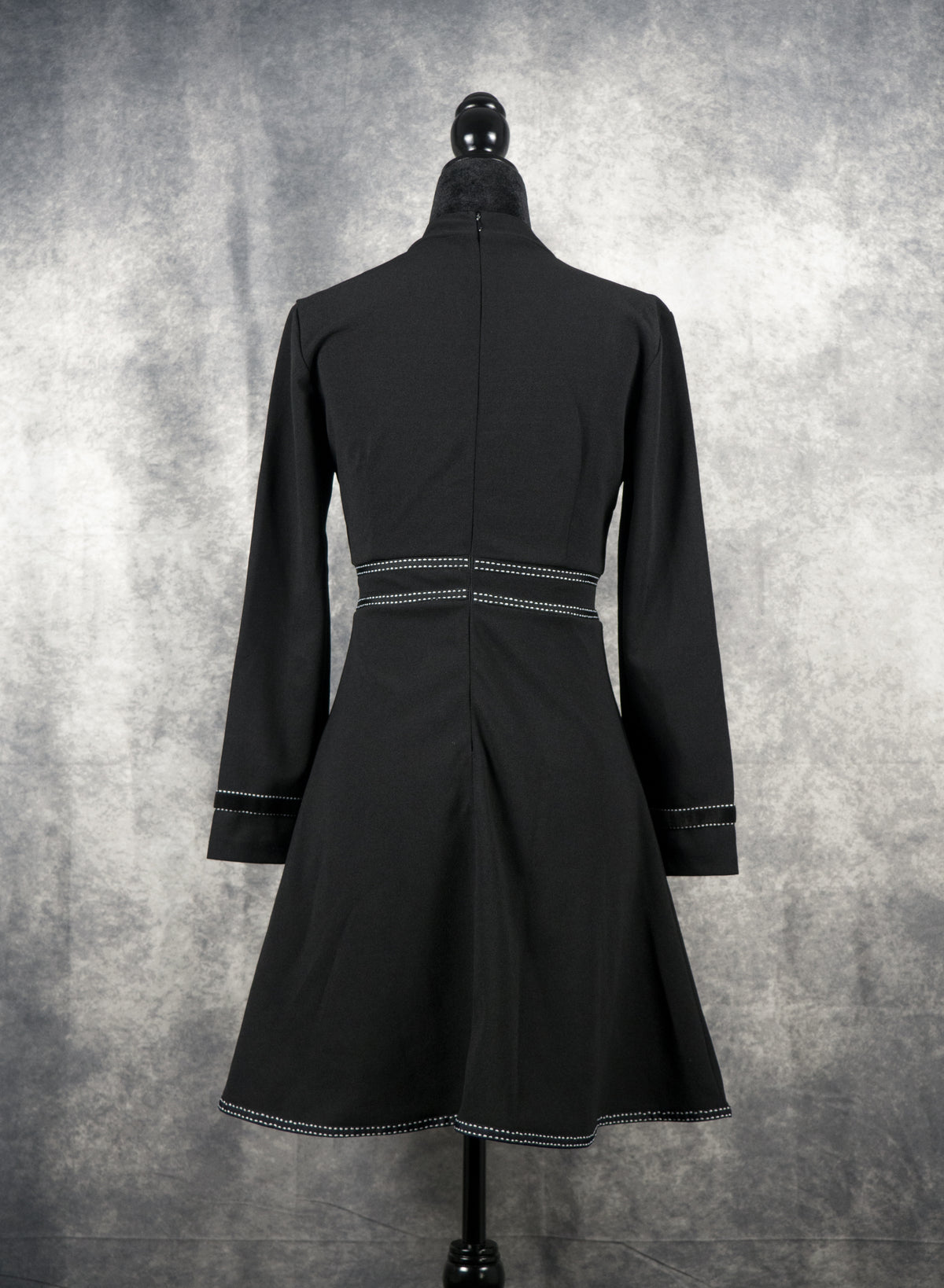 Back view of a black long-sleeve gothabilly, rockabilly, dress on a mannequin, featuring white contrast topstitch details, and a vintage fit-and-flare A-line silhouette.
