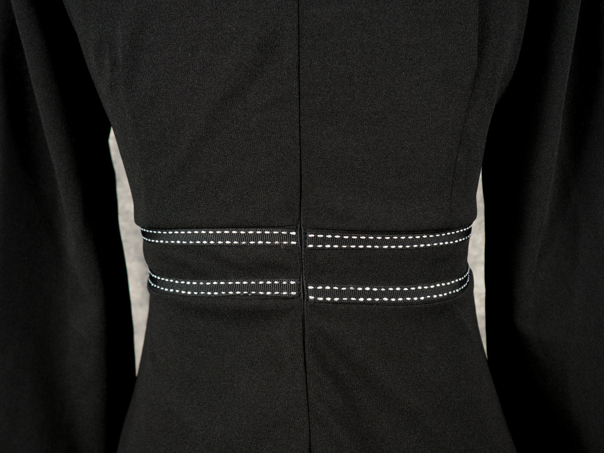 Close-up back view of a black rockabilly dress waist, showcasing horizontal white contrast topstitching details on the waistband and a clean center seam.
