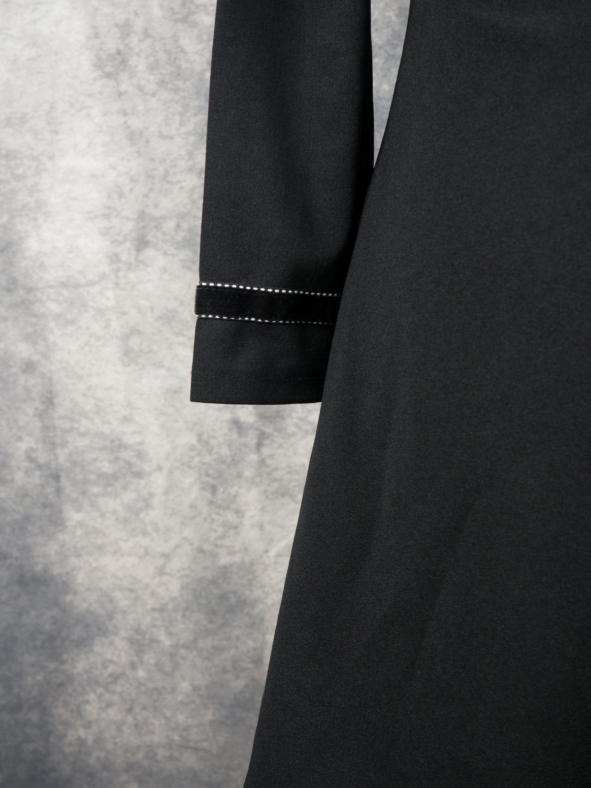 Close-up of a black dress sleeve with white contrast stitching, set against a textured gray background.