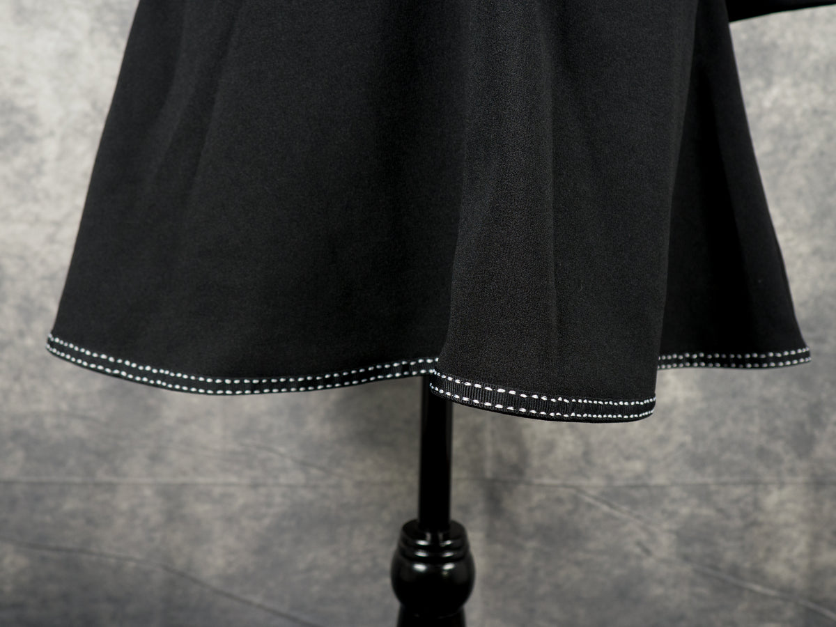 Close-up of the flared hemline on a black alternative A-line dress, featuring a neat horizontal white contrast topstitch border detail on a mannequin.
