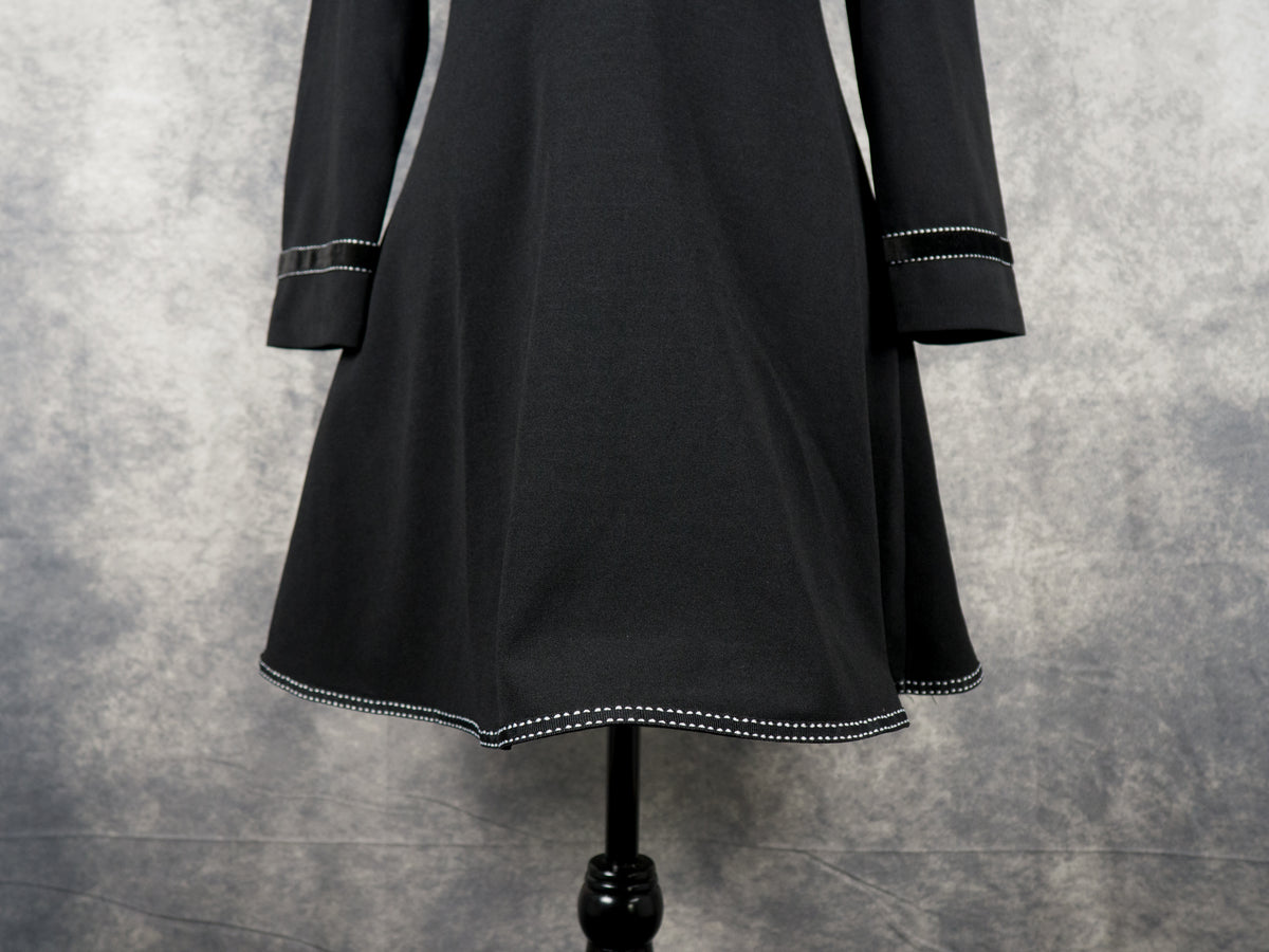 Front view close-up of a black gothabilly dress waist and long sleeves, highlighting horizontal white contrast topstitching on the waistband and matching velvet trim cuffs.
