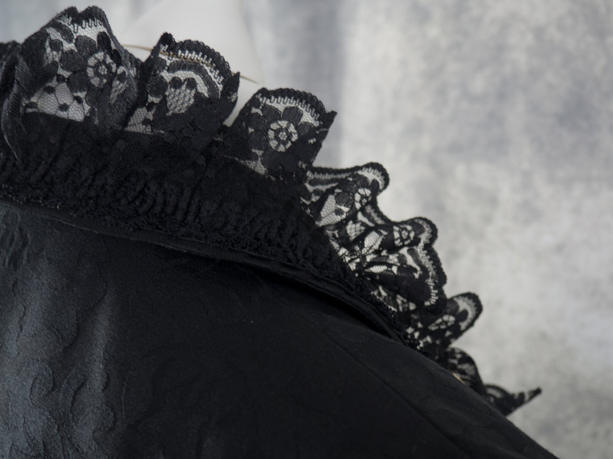 Close-up of a black fabric item with a decorative black lace trim against a textured gray background.
