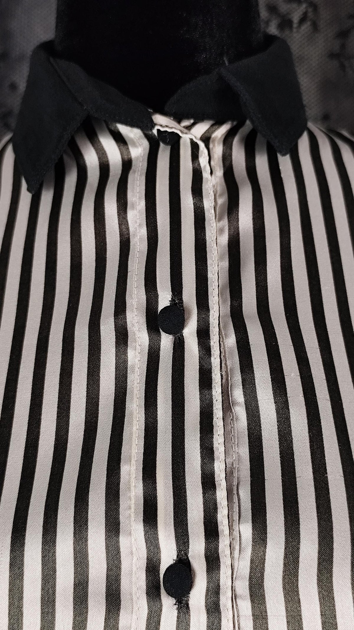 Close-up of a black and white vertically striped satin shirt on a mannequin, featuring a solid black collar and black buttons.