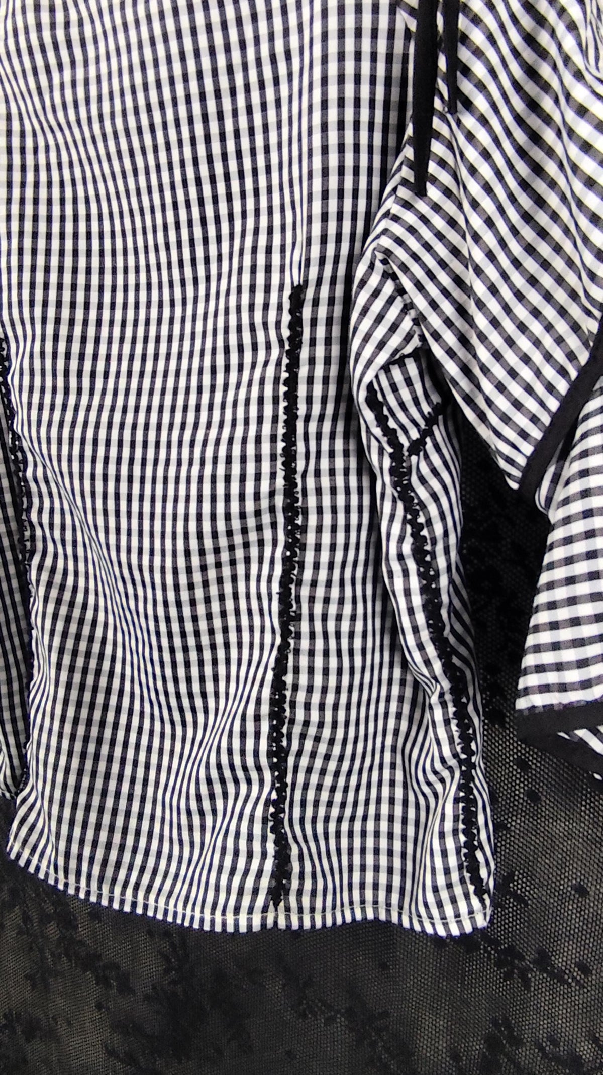 A close-up of a black and white checkered blouse, featuring vertical black lace-like trim running down the back.