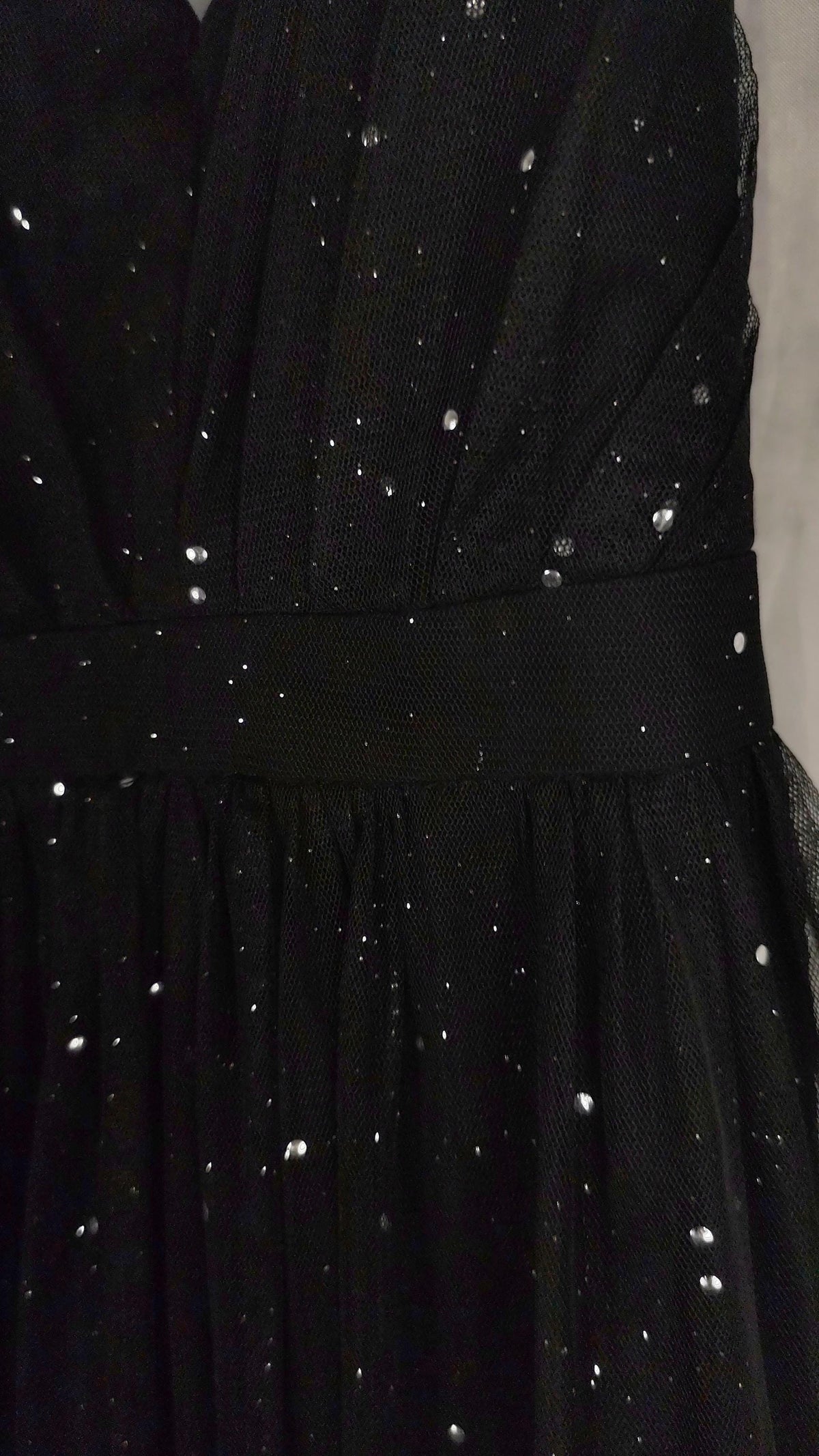 Close-up of a black dress with sheer tulle overlay and scattered silver rhinestone embellishments, featuring a defined waistband.