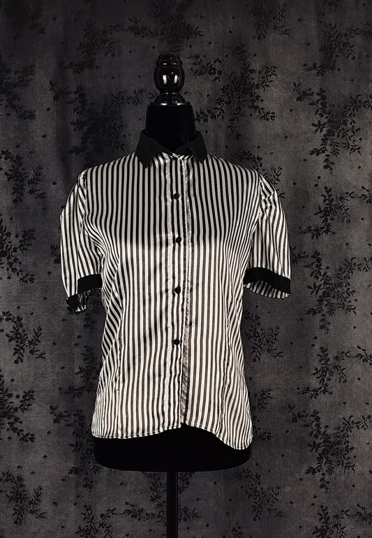Front view of a short-sleeve button-up shirt with vertical black and white stripes, displayed on a black mannequin torso against a dark textured backdrop.
