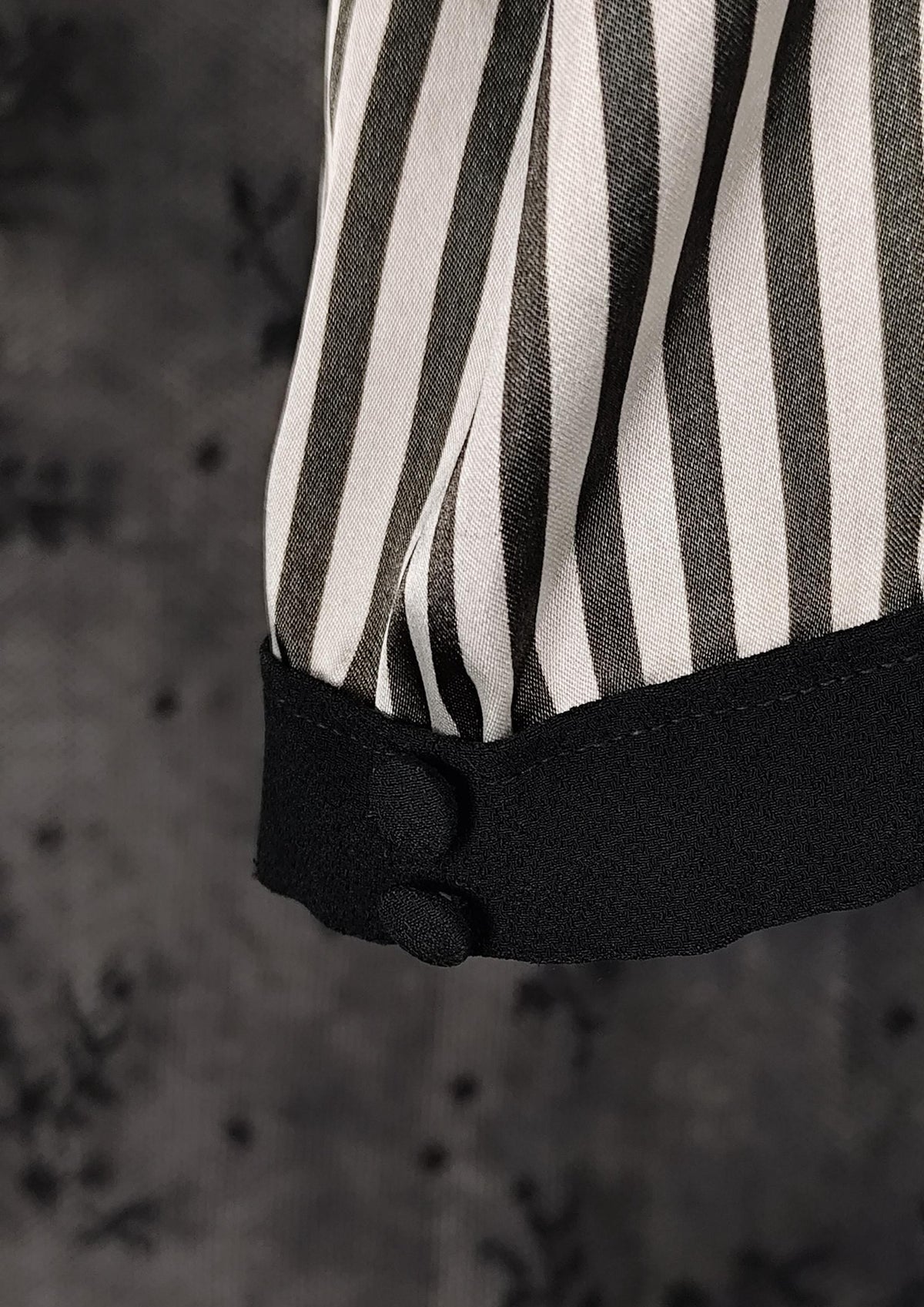 Close-up of a striped garment sleeve with black and off-white vertical stripes and a black cuff detail, set against a dark textured background.