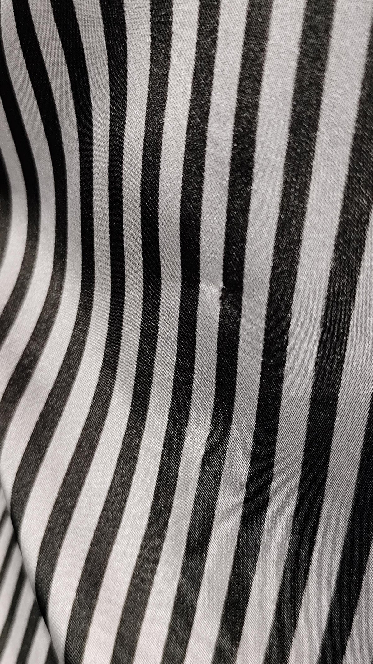 A close-up of a black and white vertically striped fabric with a visible small hole patch near the center.