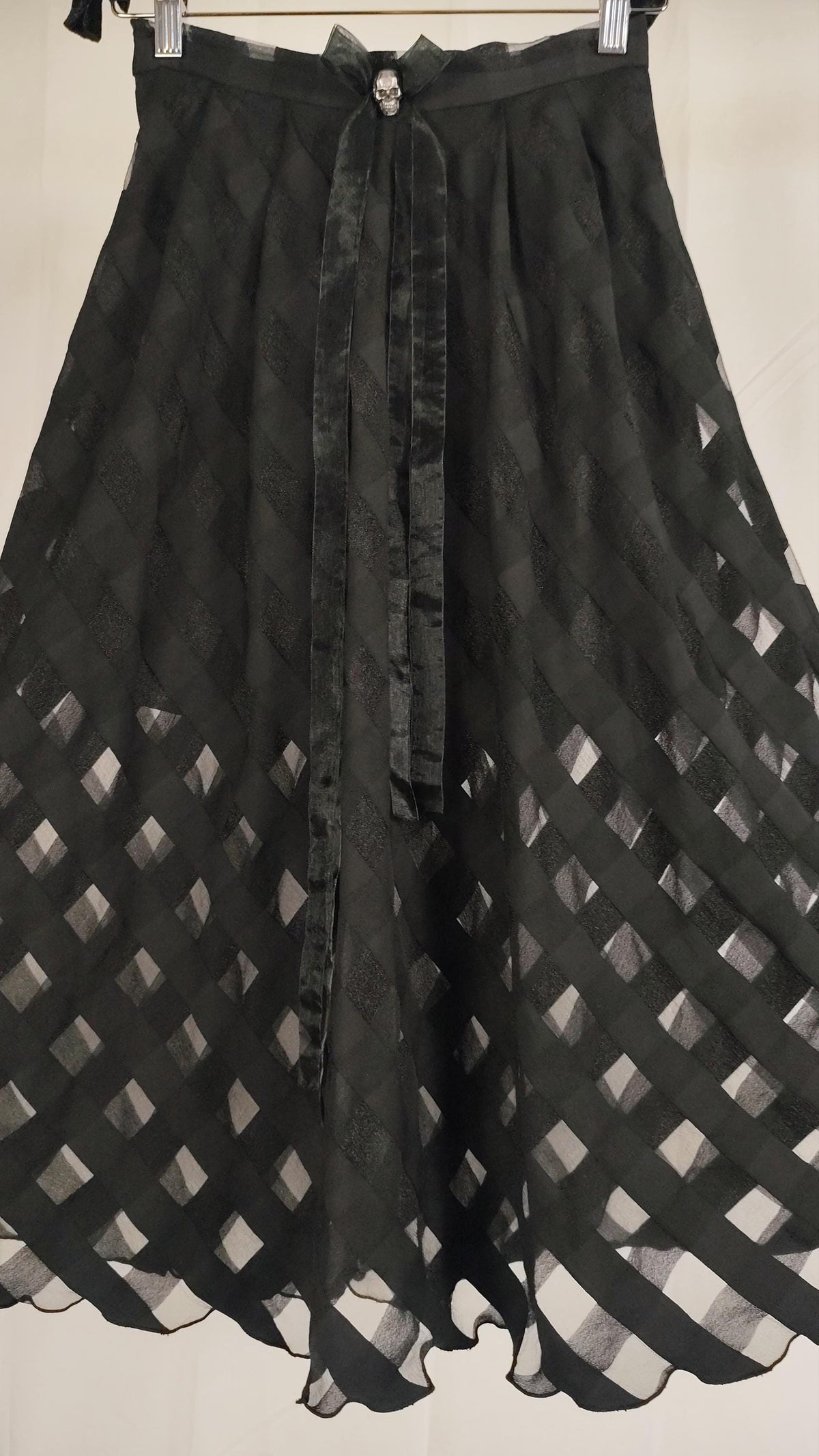 A black sheer skirt with a diamond lattice pattern and a matching organza bow with a silver metal skull, hanging against a plain light background.
