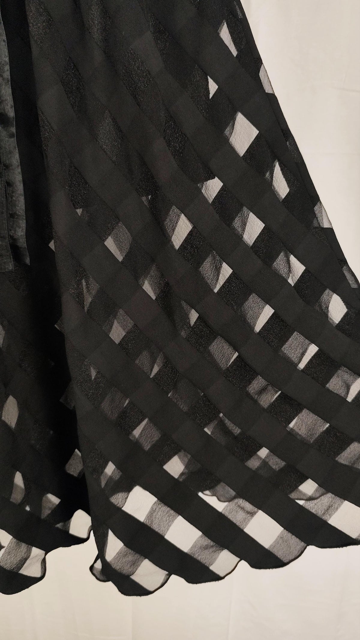 A close-up of a black sheer skirt with a repeating diamond lattice pattern, draped against a light off-white background.