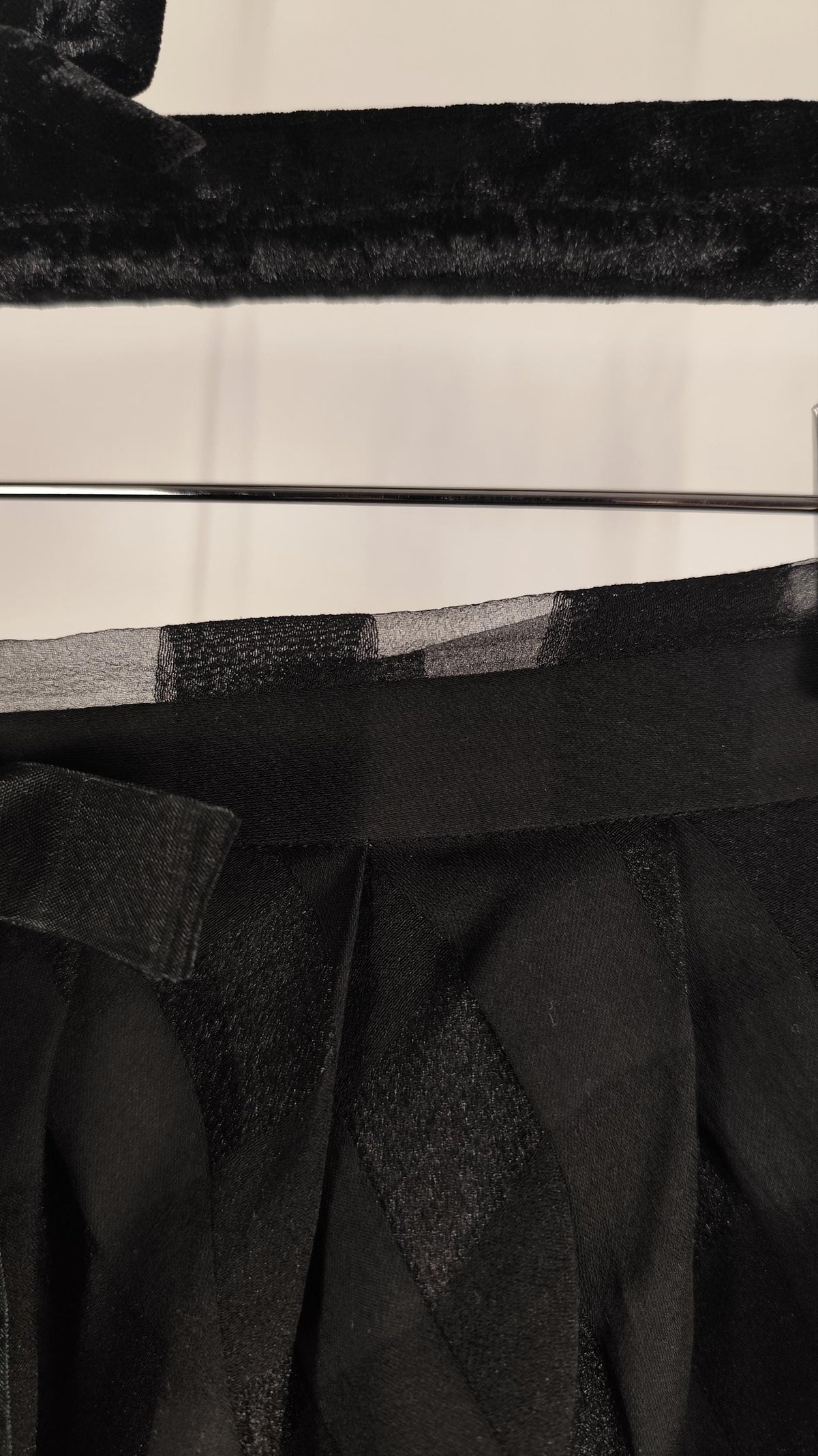 Close-up detail of a black textured skirt, showing a wide black waistband with a matching fabric belt and pleated black skirt or dress material.