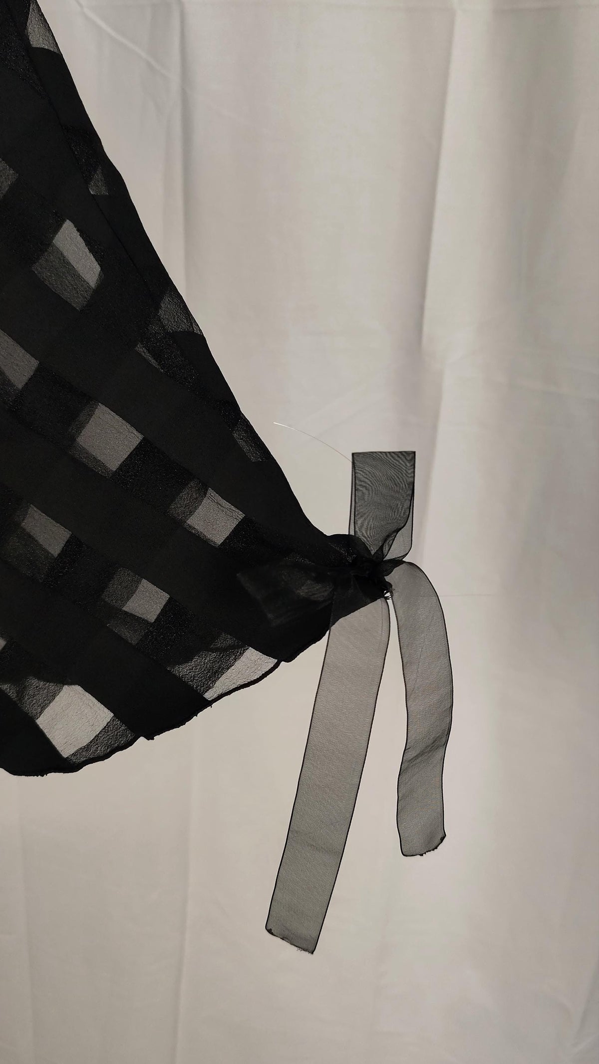 A close-up of a black sheer skirt likely a with a wide black organza ribbon against a white fabric backdrop.