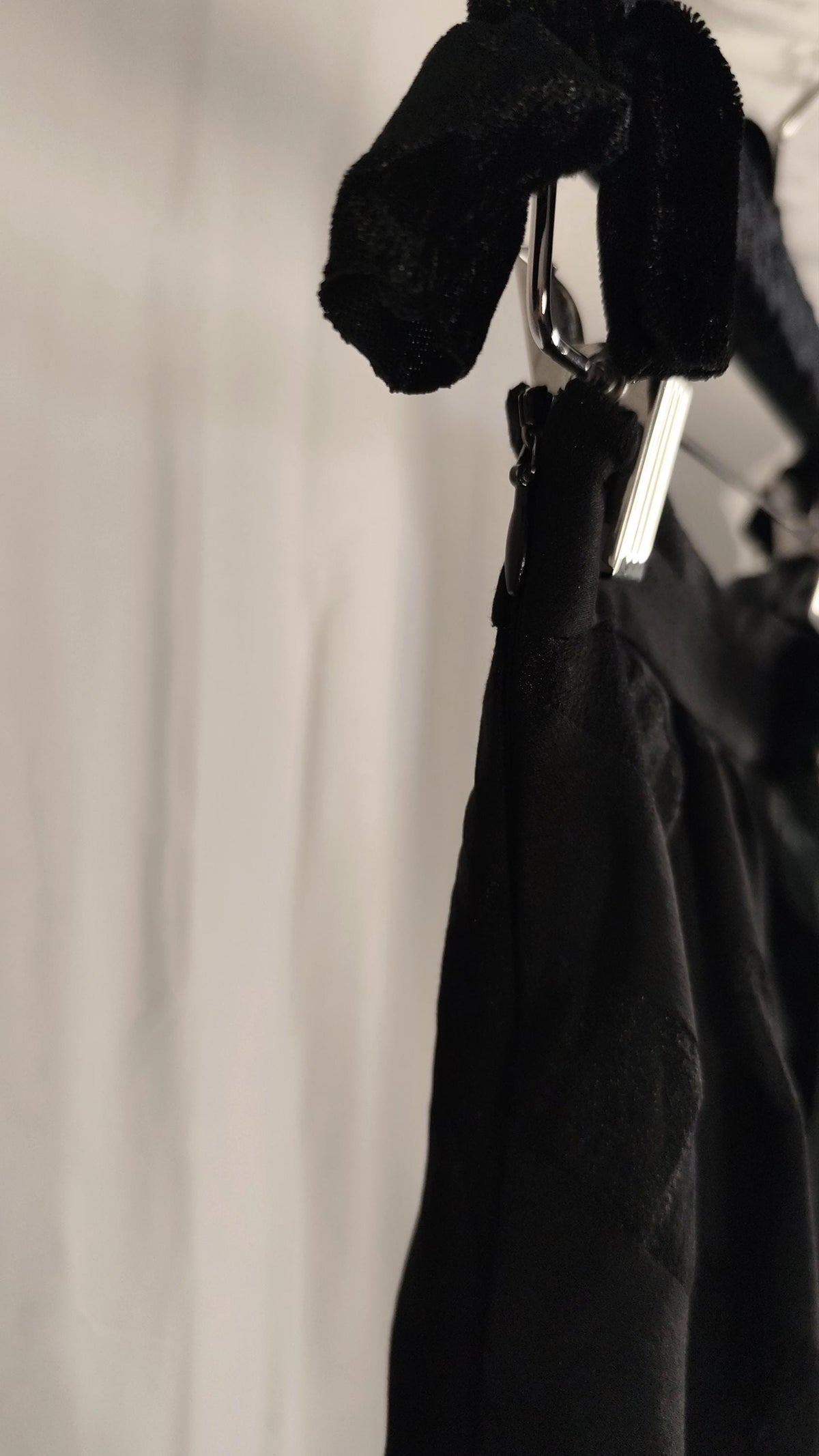 A close-up of a hidden zipper of a black skirt hanging on a black fuzzy hanger against a light gray fabric backdrop.