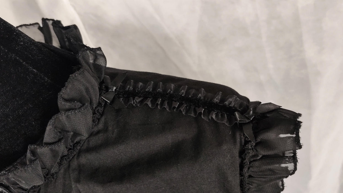 Close-up of a black ruffled and sheer mesh trim and a textured fabric background.