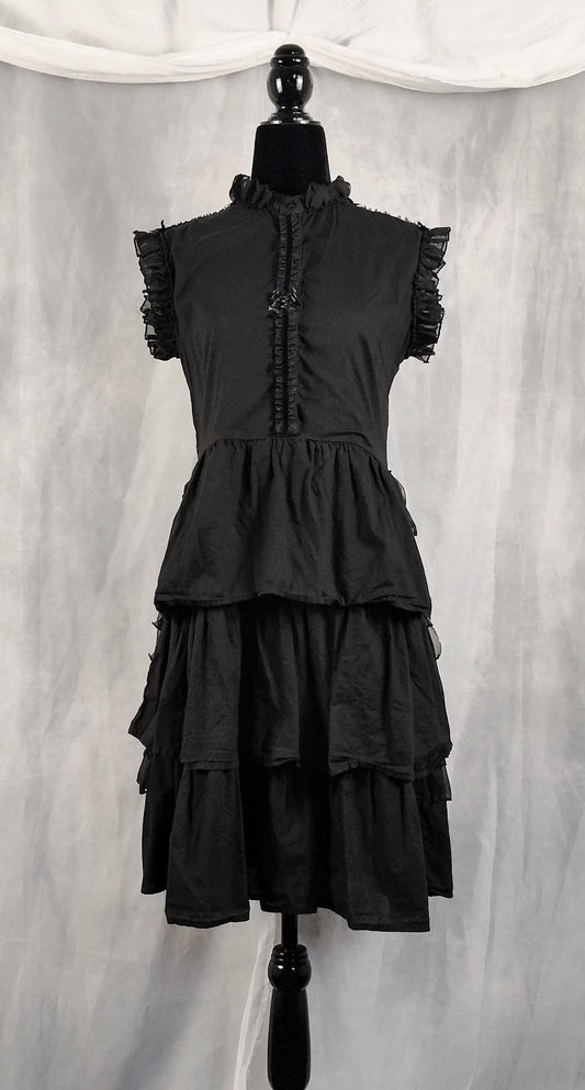 Front view of a black tiered ruffled dress displayed on a black mannequin against a gray draped fabric backdrop.