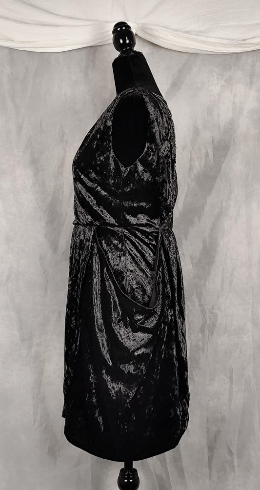 A sleeveless black crushed velvet dress displayed on a black mannequin torso against a gray draped fabric backdrop.