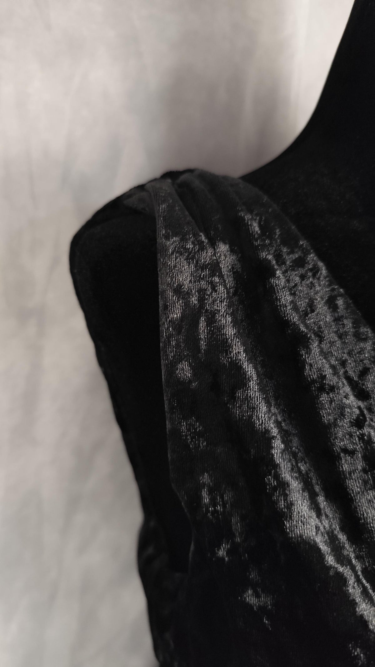 Close-up of a black velvet dress over a dark garment or mannequin, showing the soft textured sheen against a light neutral background.