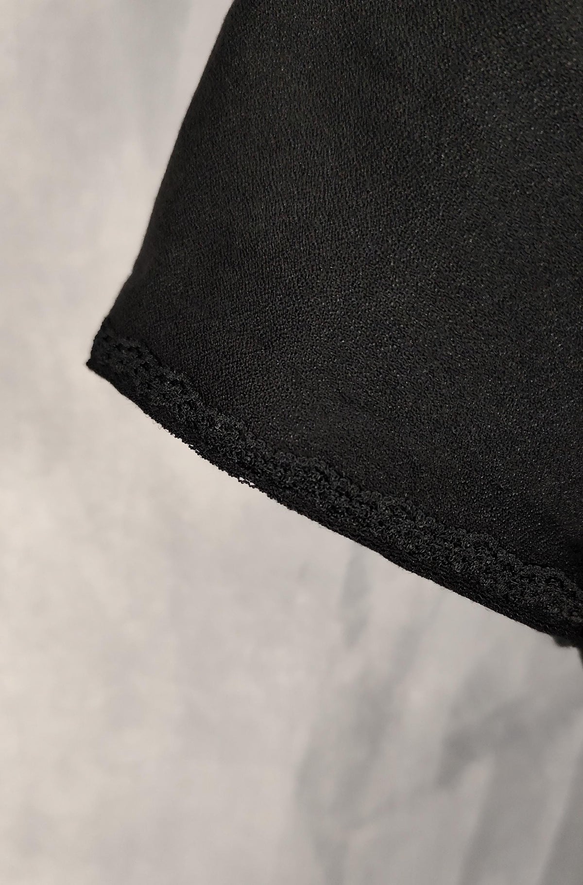 Close-up of a black short-sleeve with a lace trim against a light gray background.