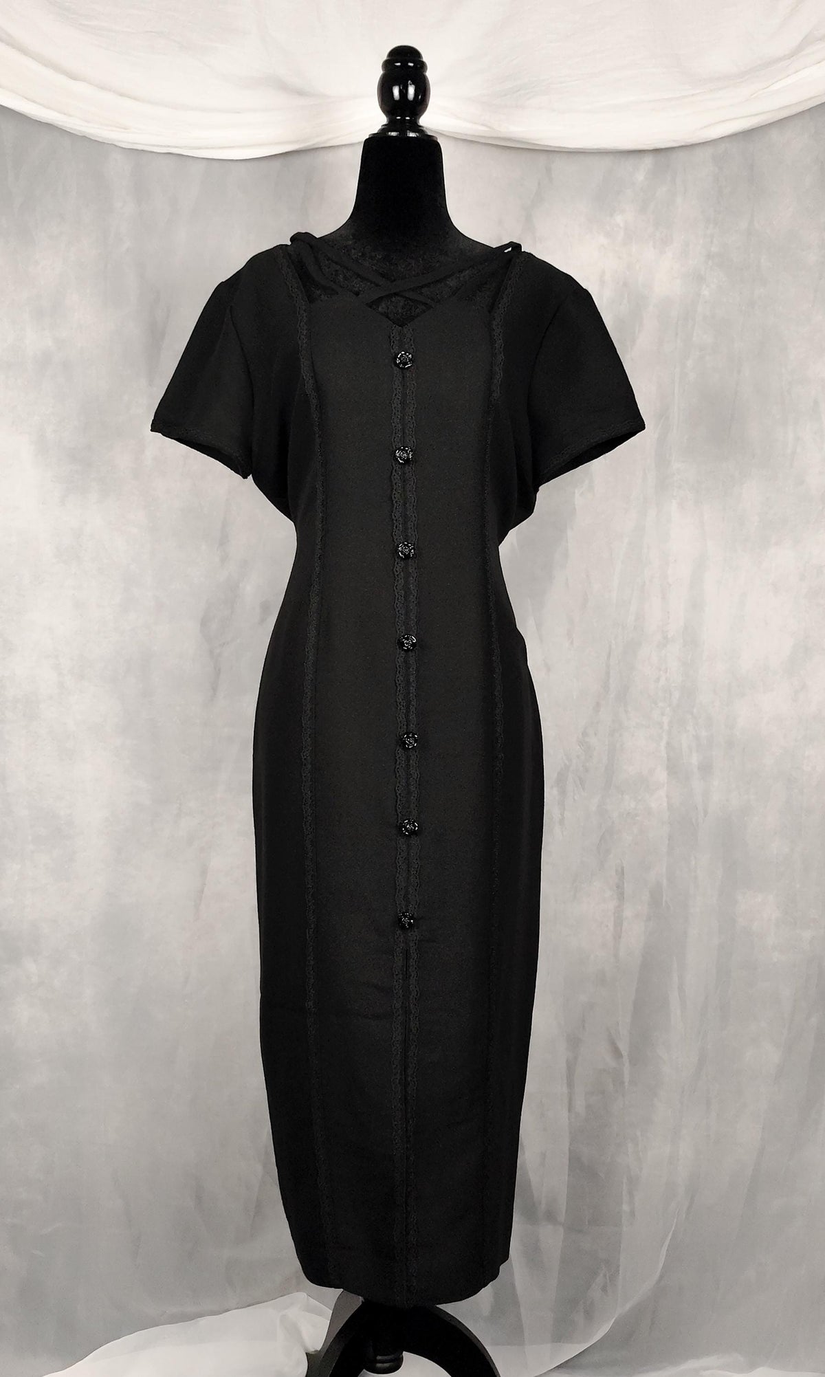 Front view of a black short-sleeve vamp midi dress displayed on a black mannequin against a gray draped fabric backdrop.