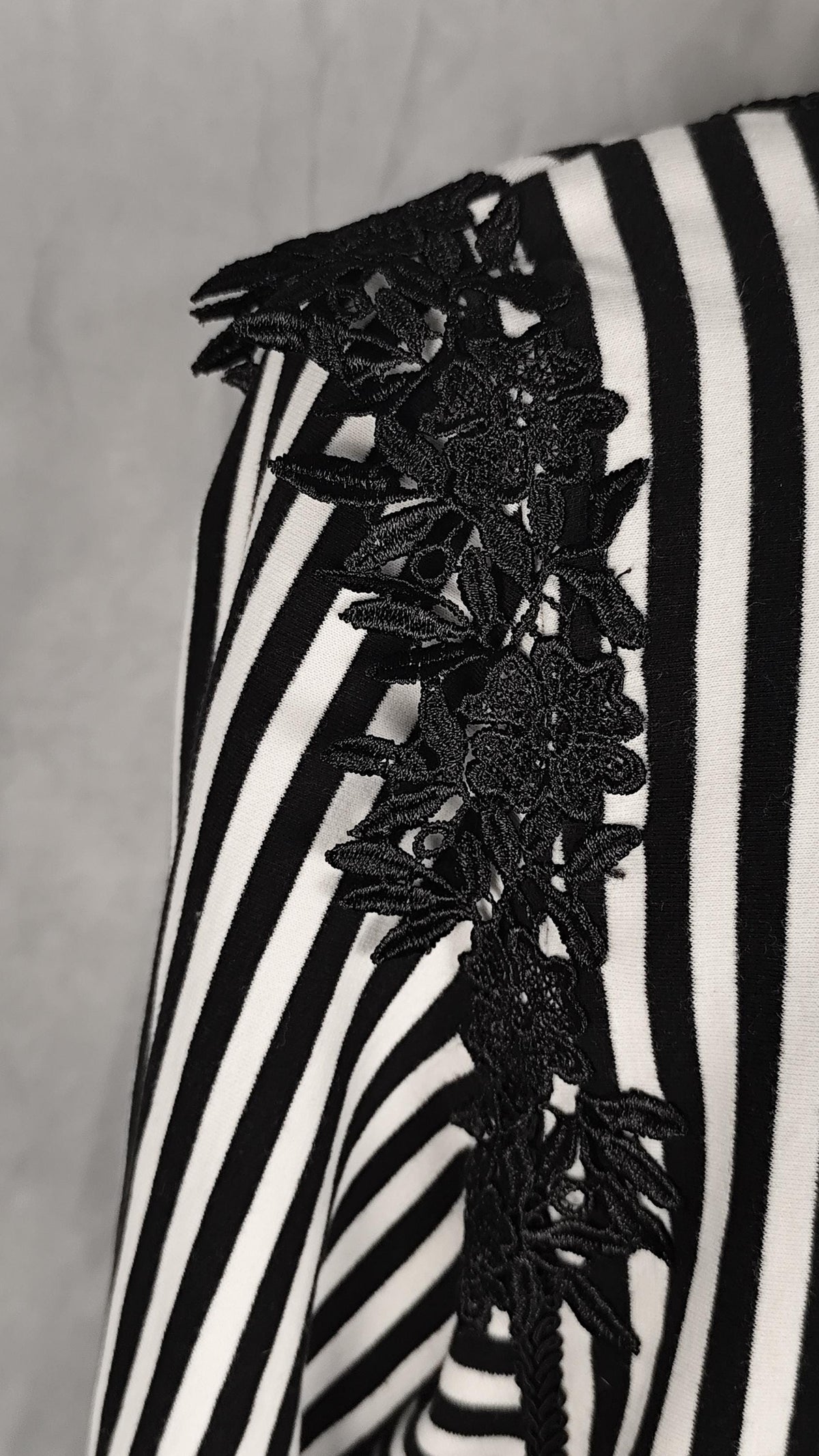 Close-up of a black and white striped bolero's shoulder with a prominent black floral lace applique detail along one side.