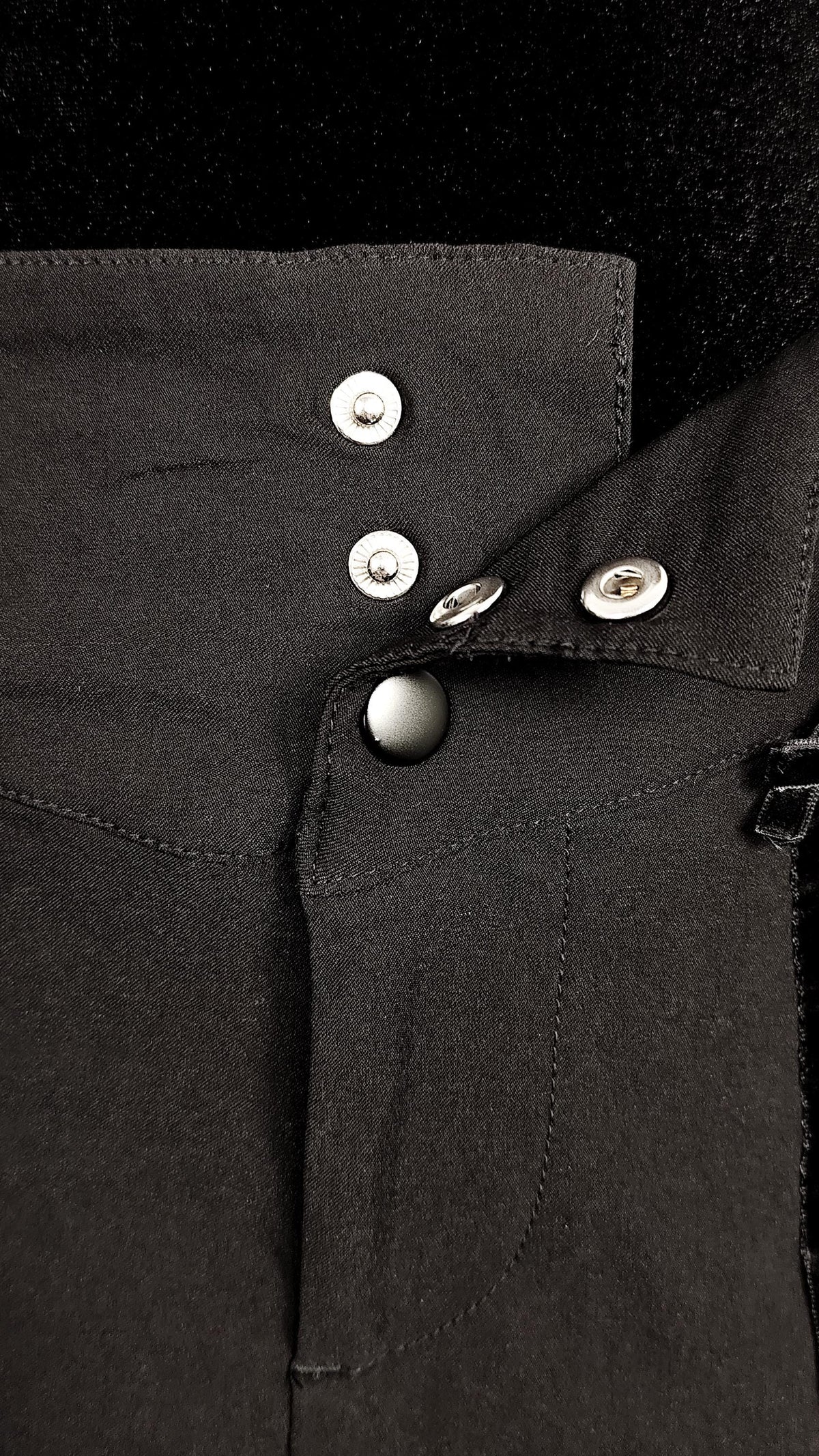 Close-up of a black skirt with black and sikver metal snap buttons and a zipper detail on a black background.
