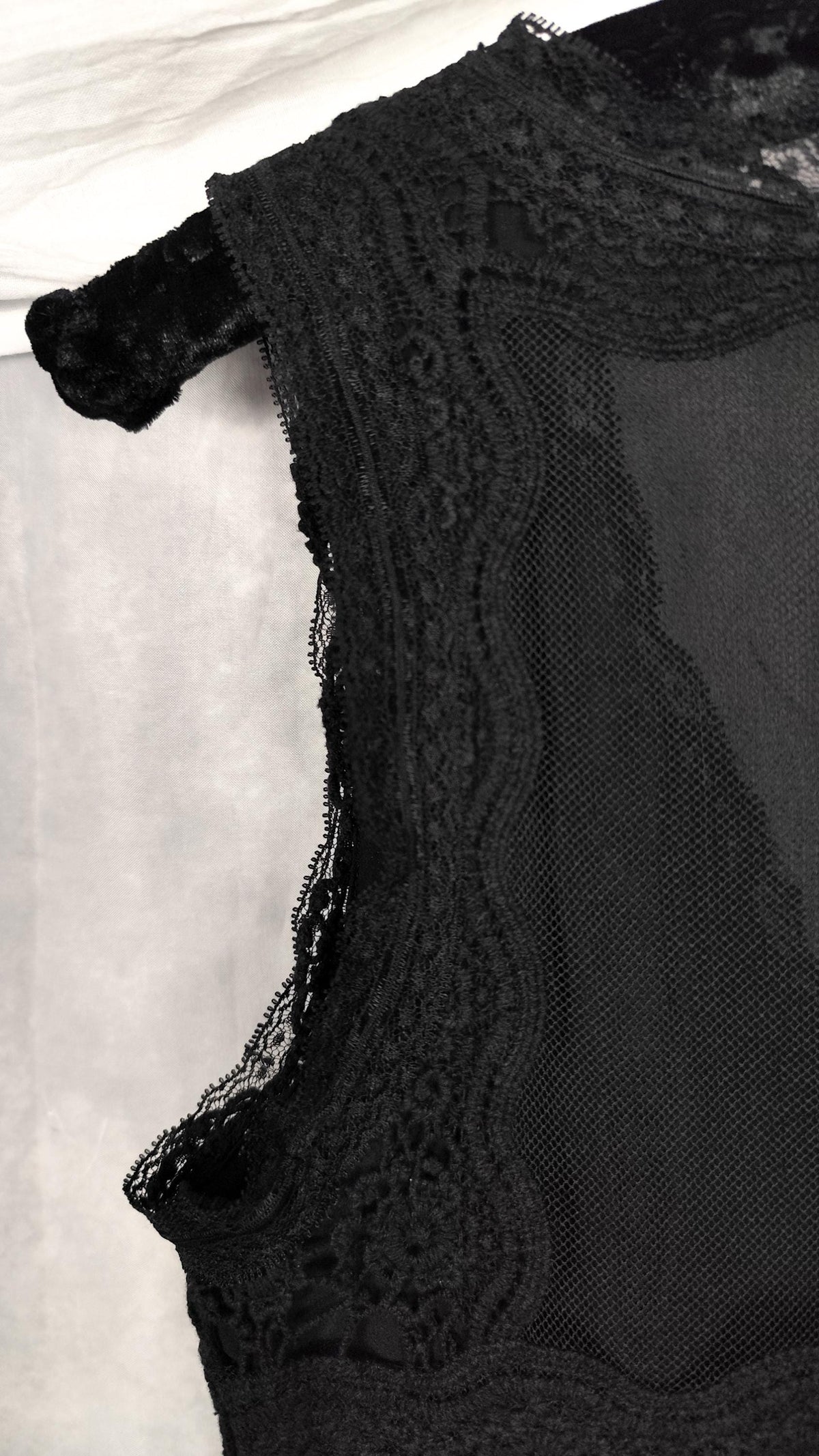 Close-up of a black lace and mesh midi dress flat on a light fabric background, showing the textured lace trim and sheer fabric.