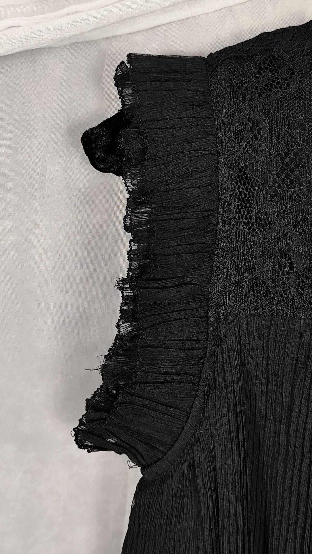 Close-up of a ruffled cap sleeve of a black dress, laid flat on a light gray surface.