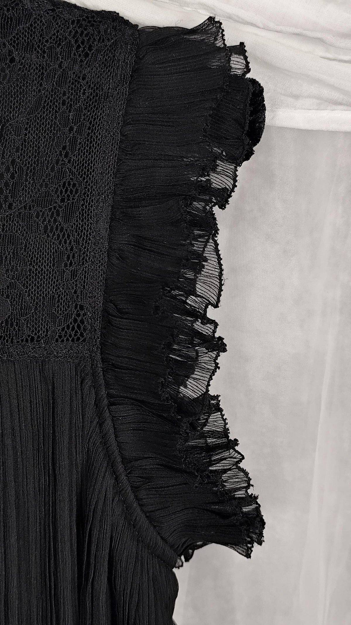Close-up of a ruffled cap sleeve of a black dress, laid flat on a light gray surface.