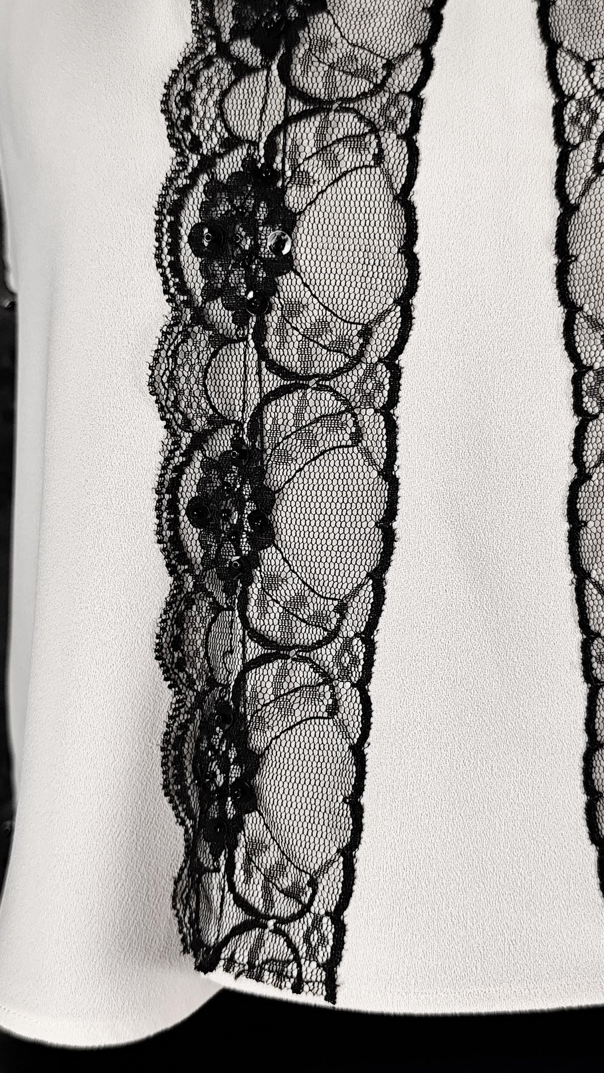 Close-up of a white garment featuring a prominent vertical black lace panel with scalloped floral embroidery and mesh detailing.