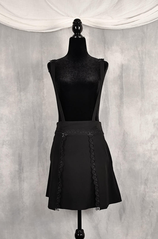 Front of high knee black skirt with removable straps and lace and satin bows details.