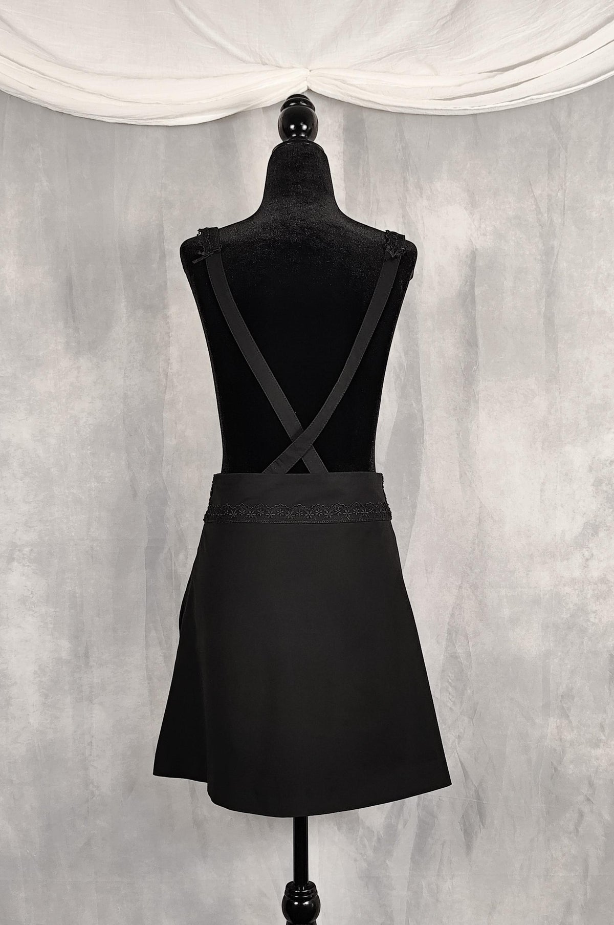Back view of a high knee black skirt with removable straps and lace and satin bows details.