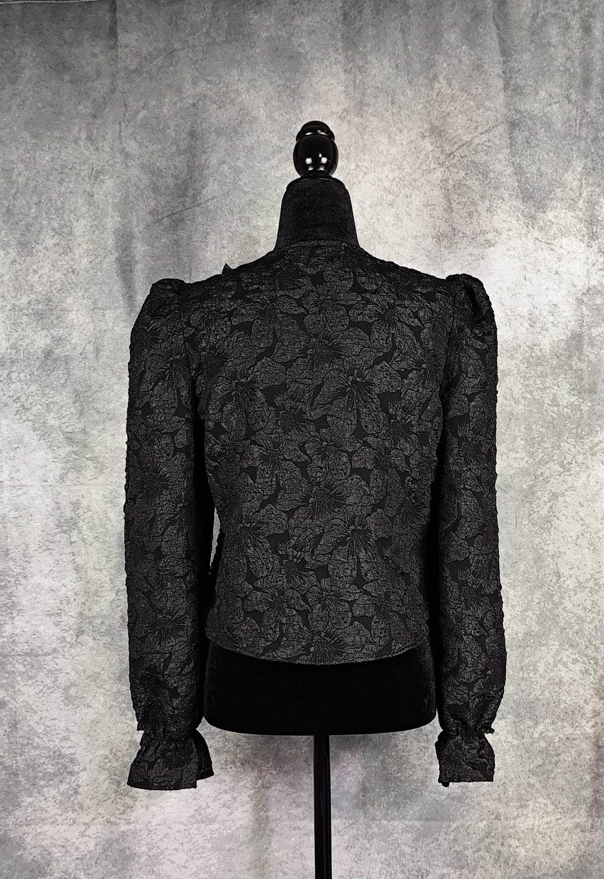 Back view of a black floral brocade blouse with black pearl-shaped buttons and braid trim.