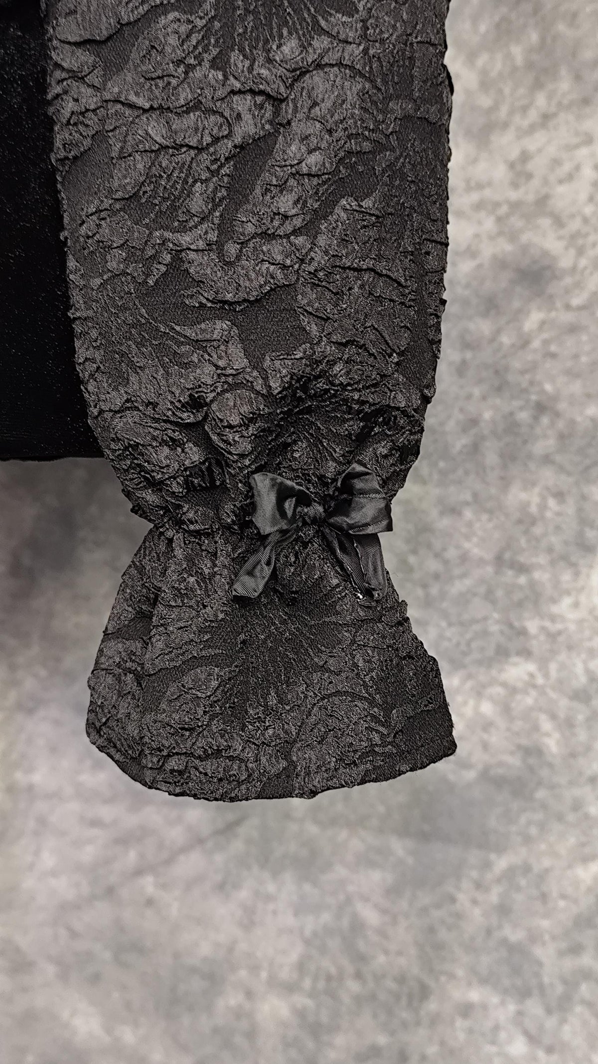 Close-up of a cuff with bow, from a black brocade longsleeve blouse.