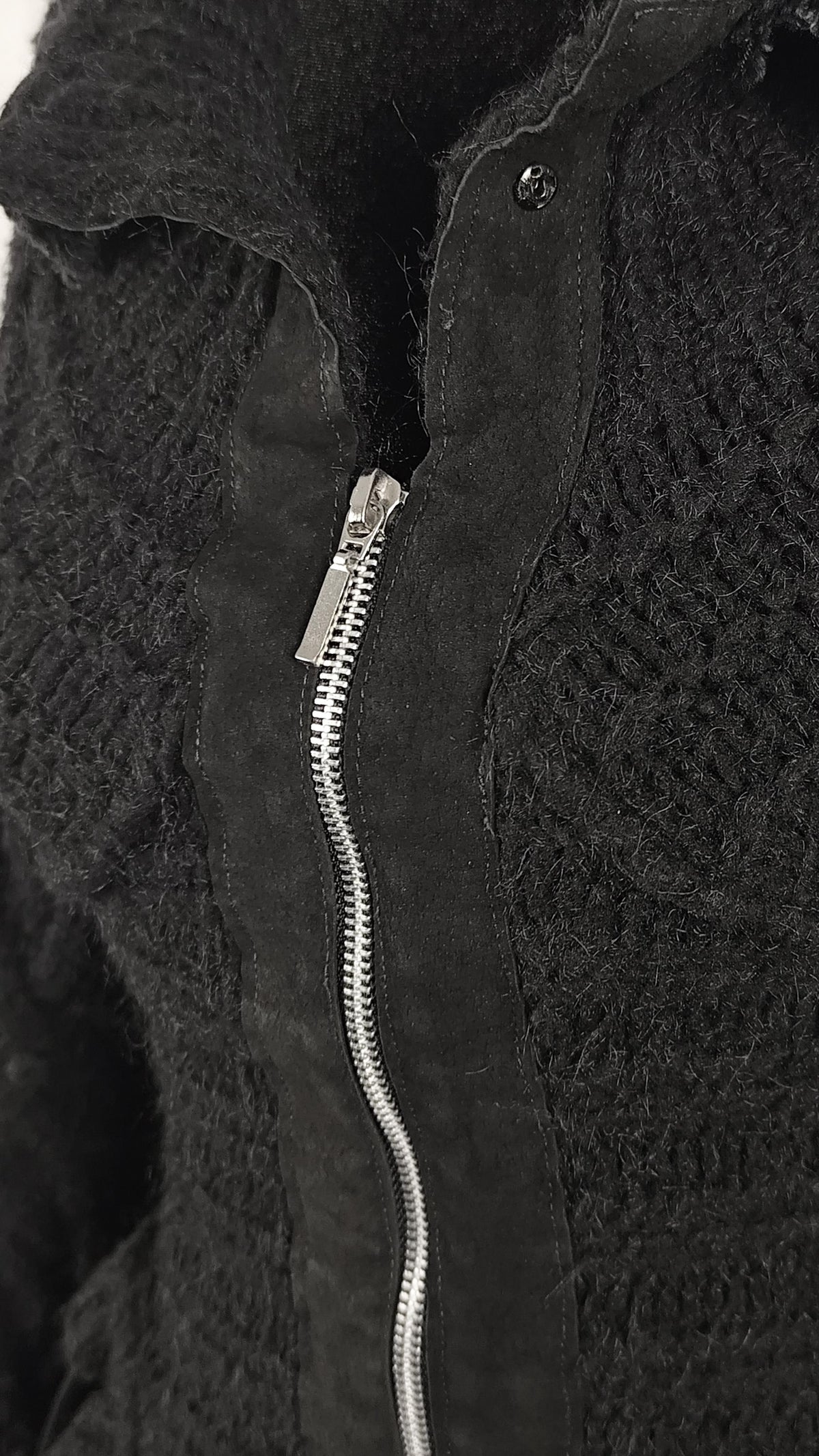 Close-up of a black textured nkint jacket with a silver zipper and a small metal snap button closure.