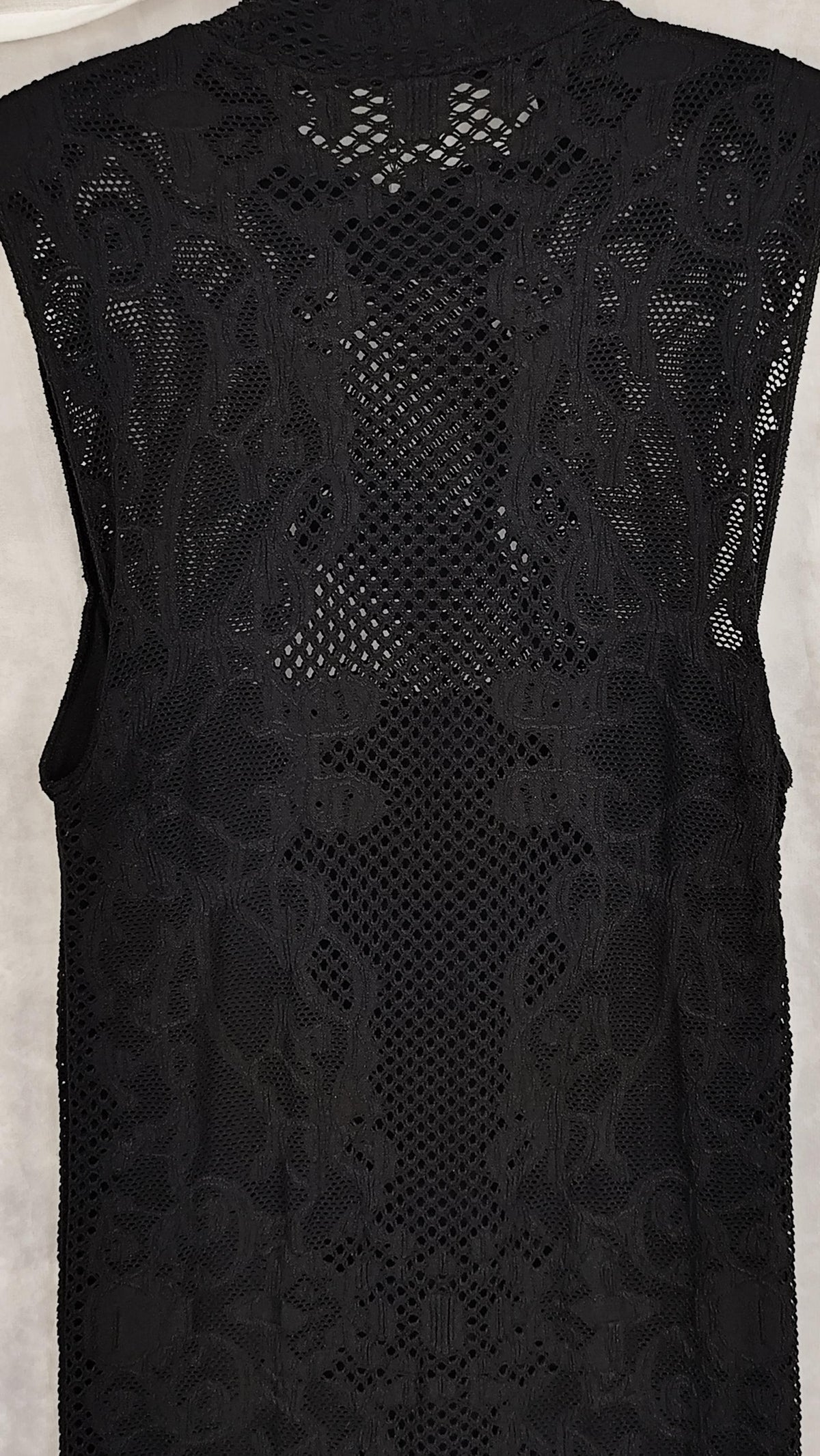 Close-up of a black sleeveless lace dress with a sheer mesh pattern, shown on a light gray background.
