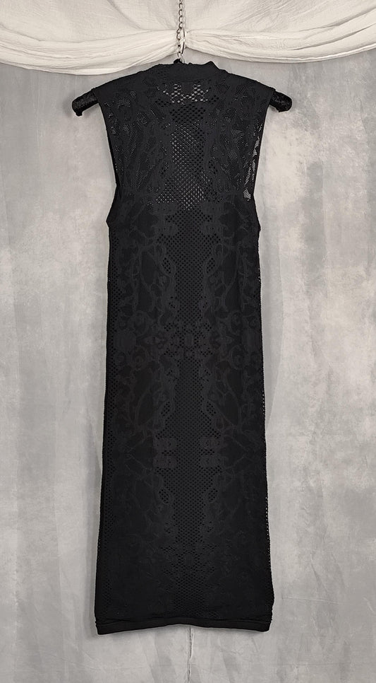 Front view of a sleeveless black midi dress with a sheer floral lace overlay and a high mock neck, hanging on a hanger against a textured gray backdrop.