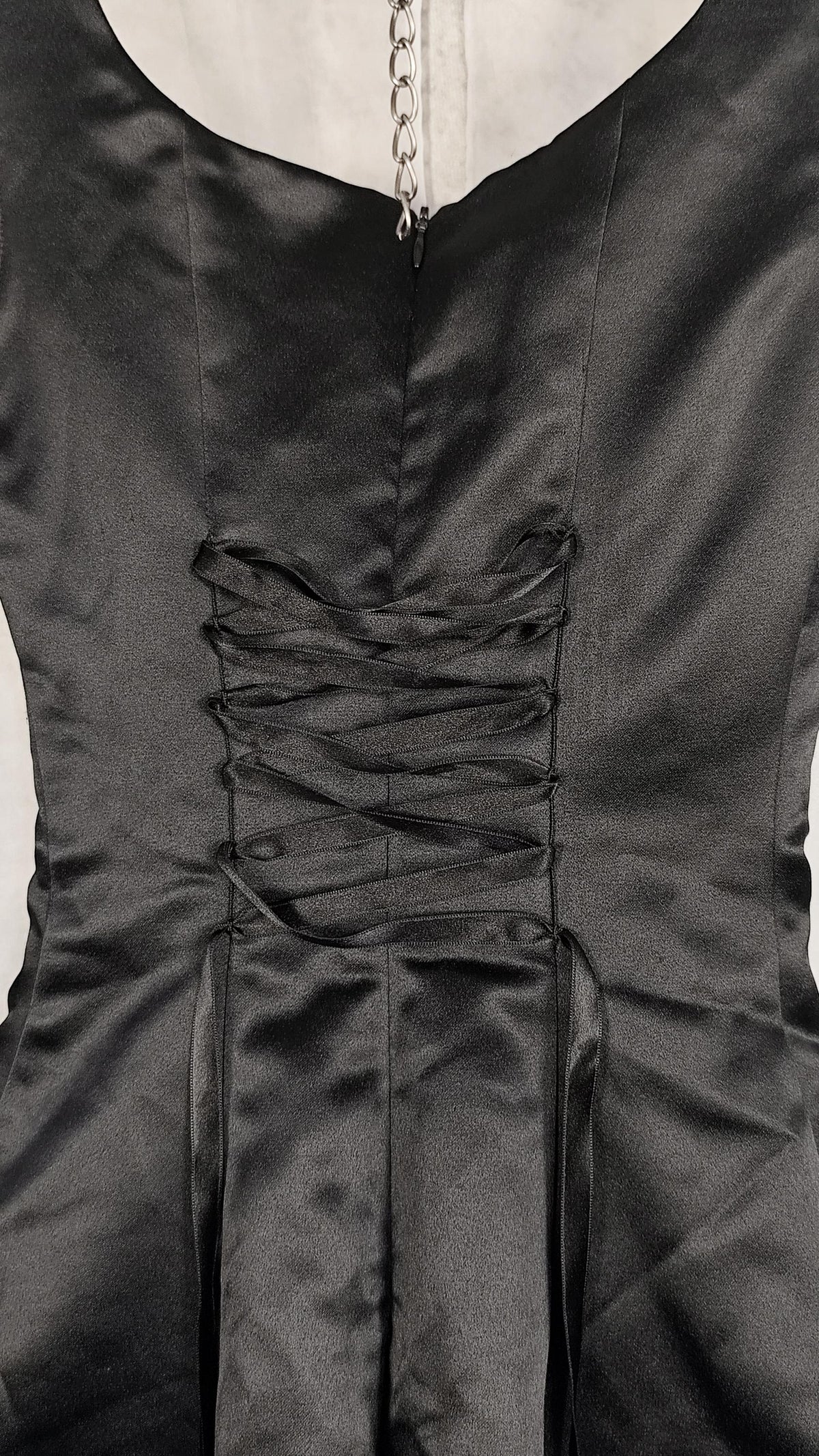 Close-up of a black satin dress with a lace-up corset-style back detail and a silver chain at the neckline.
