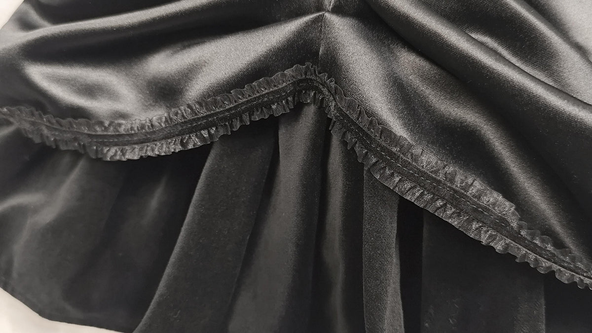 Close-up of black satin andvelvet fabric from a dress with a ruffled trim detail along the edge.