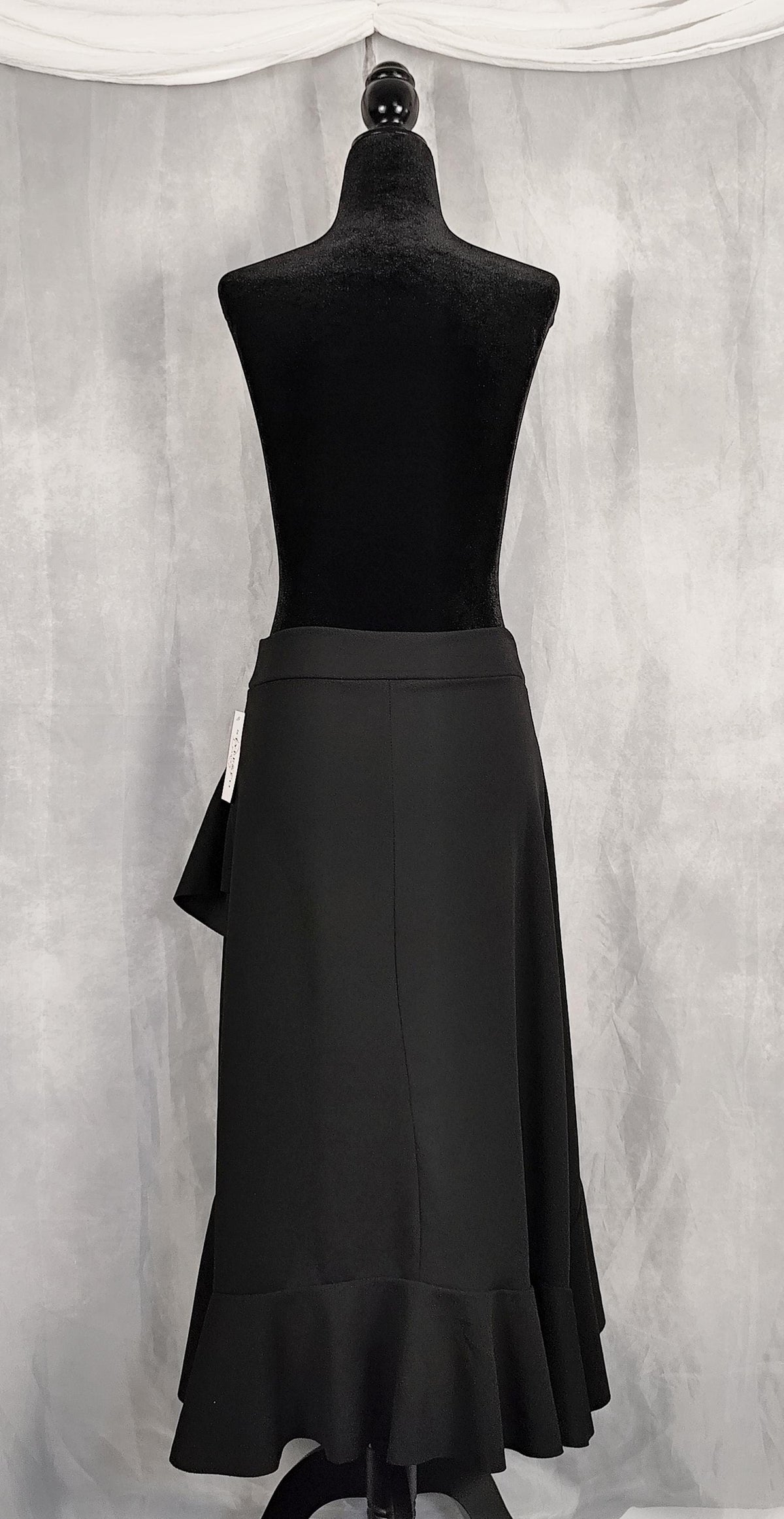 Back view of a black midi skirt displayed on a black dress form mannequin against a textured gray backdrop.