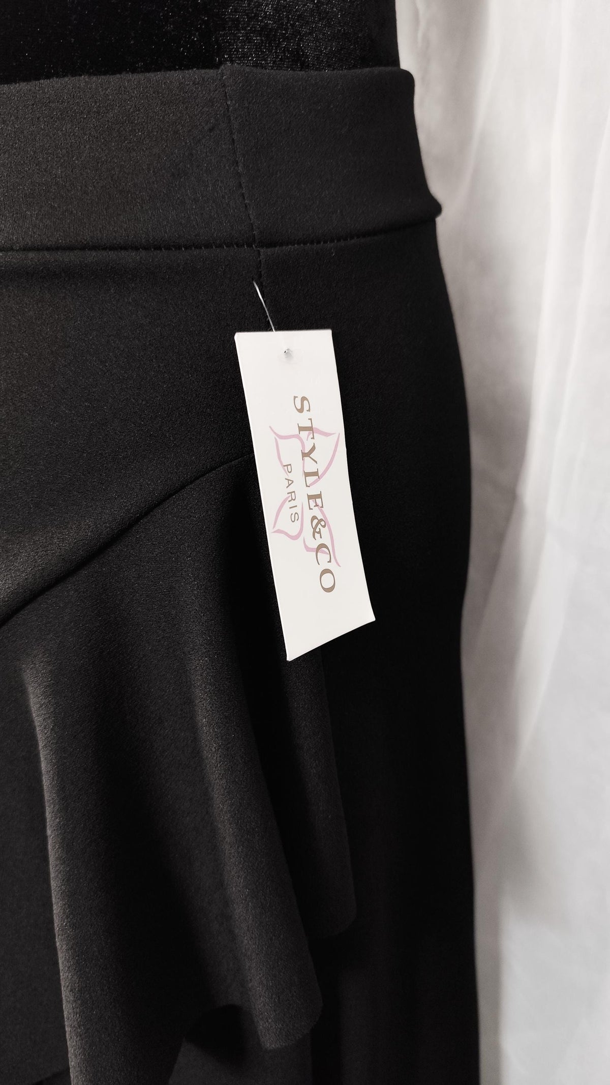 Close-up of a black skirt with a ruffled overlay and a tag hanging from the waistband, showing the brand name 'STYLE & CO PARIS' in pink script.