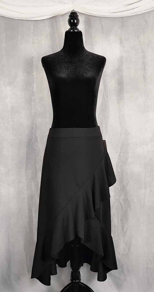 Front view of a black ruffled wrap-style skirt displayed on a black mannequin torso against a textured gray backdrop with draped white fabric at the top.