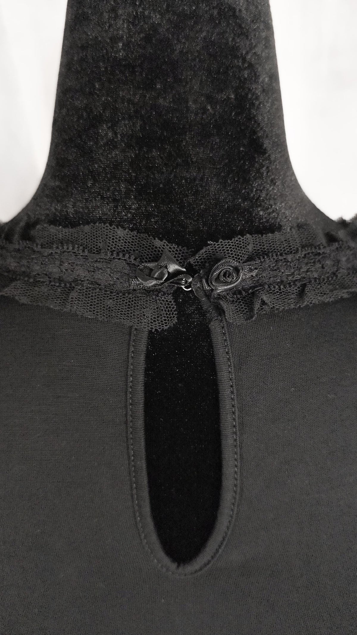Close-up of a black top neckline with a keyhole cutout, ruffled trim, and two decorative buttons on a mannequin.