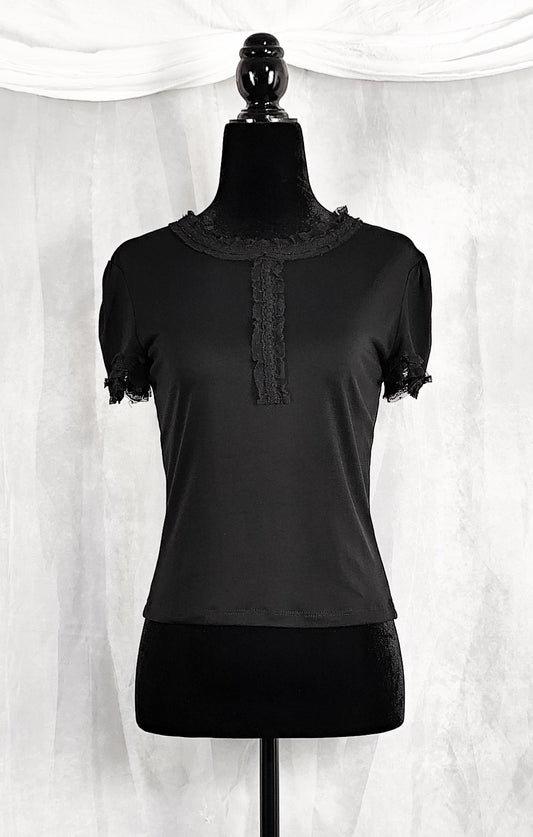 Front view of a black short-sleeve top with lace trim at the collar and sleeve cuffs, displayed on a black dress form mannequin against a white draped fabric backdrop.