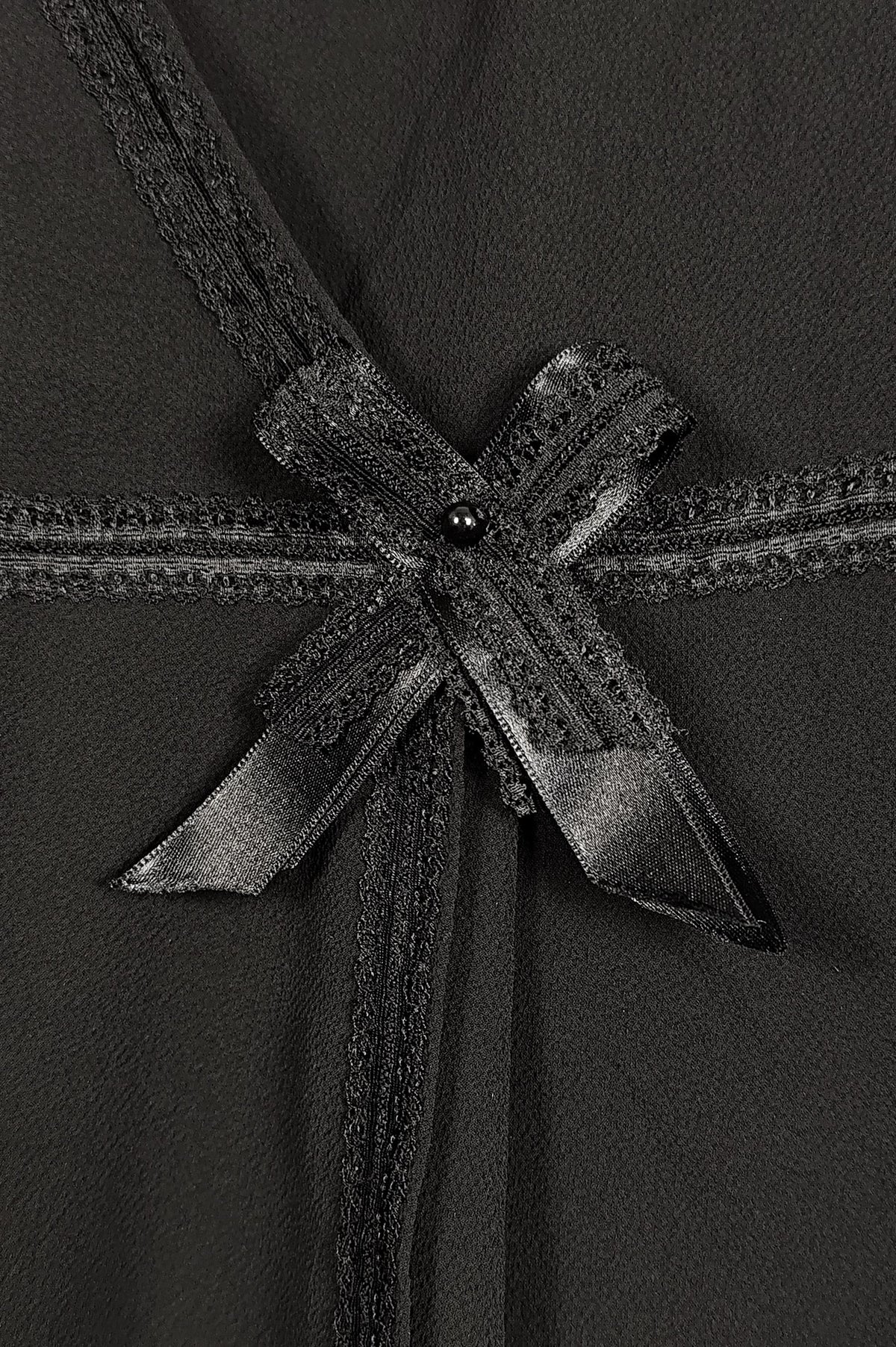 Close-up of a black wrap-style dress with a wide satin ribbon tied into a bow at the waist, featuring textured trim and a small dark bead accent.